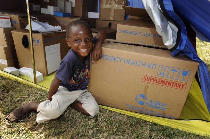 Ein Junge sitzt in einem Lager in Haiti zwischen Emergency Health Kits.
